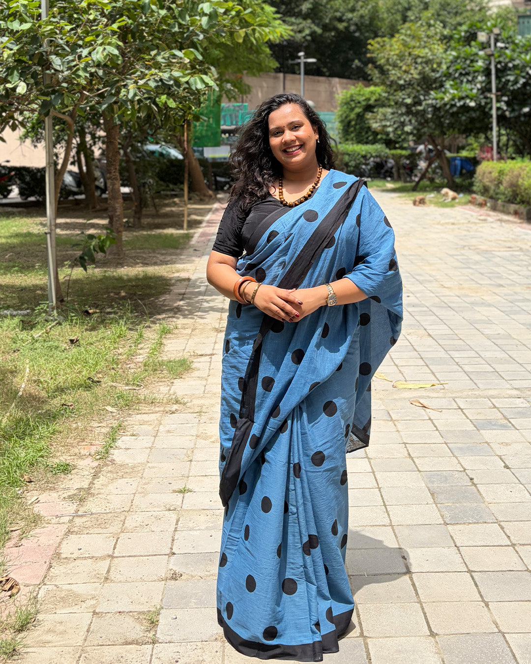 Model wearing the blue and black polka dot handwoven cotton saree outdoors with a black blouse by House of Ojasvi