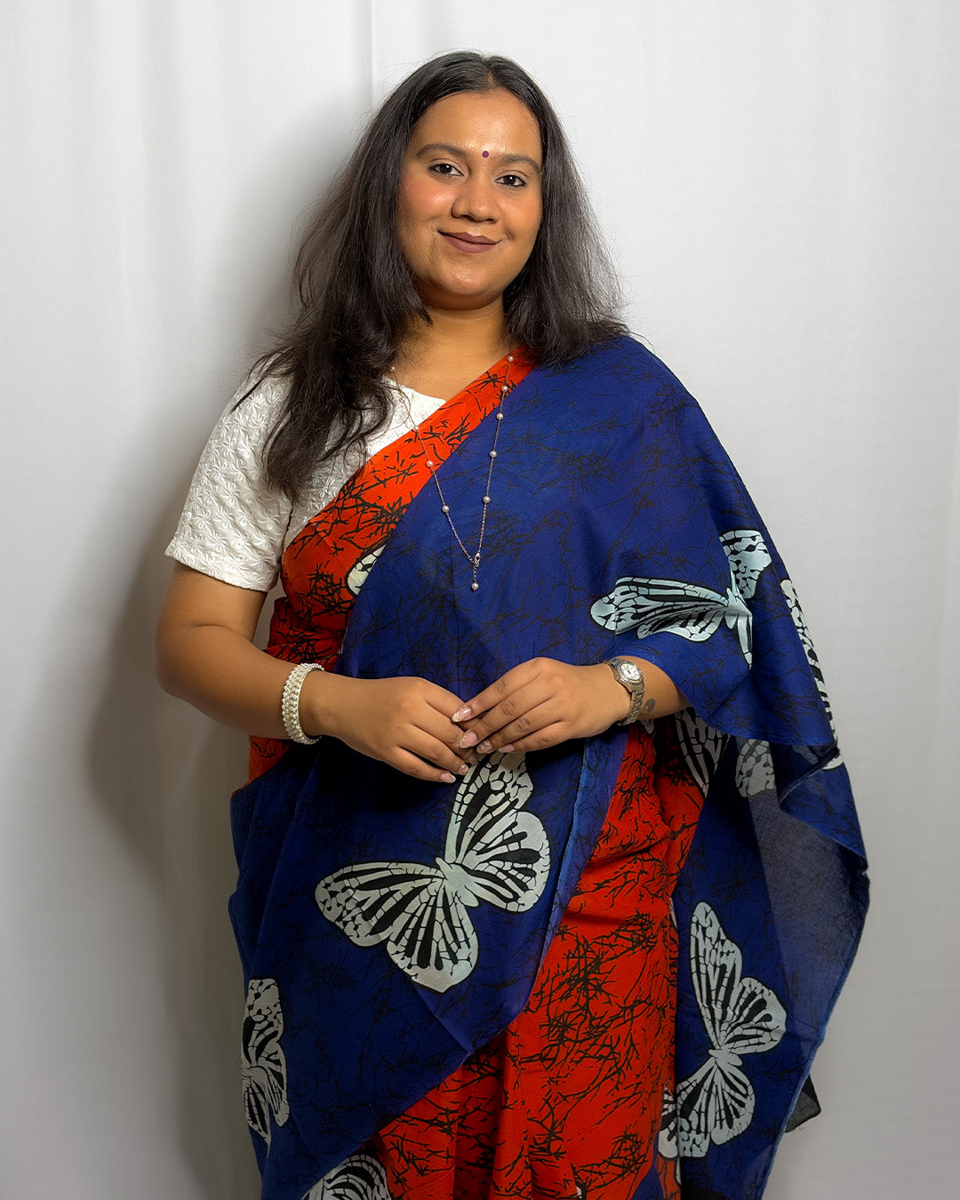 Front view of the royal blue and orange butterfly print cotton handwoven saree styled with a white blouse and pearl jewellery