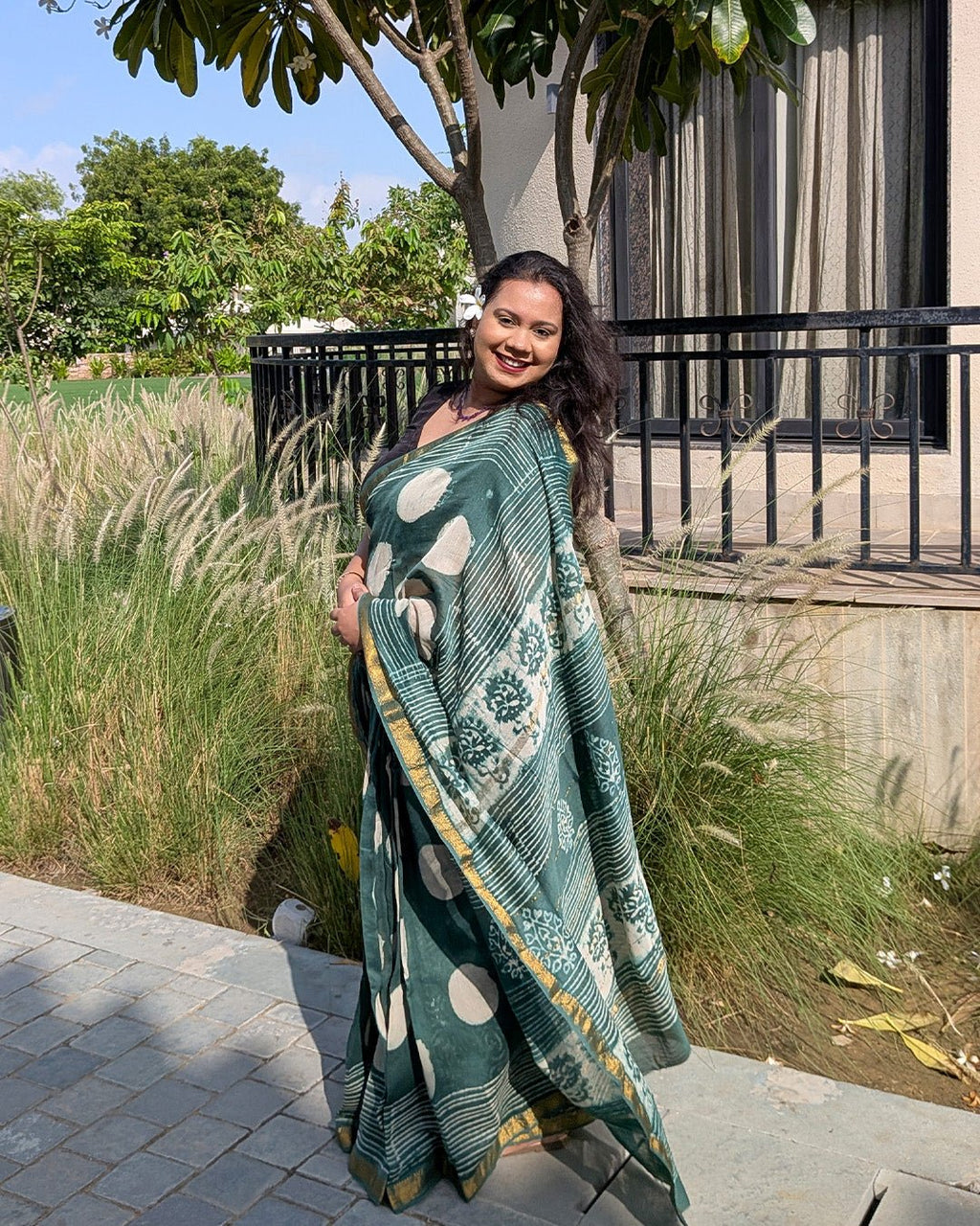 Model posing on stairs wearing the dark green polka dot handwoven Maheshwari saree by House of Ojasvi.