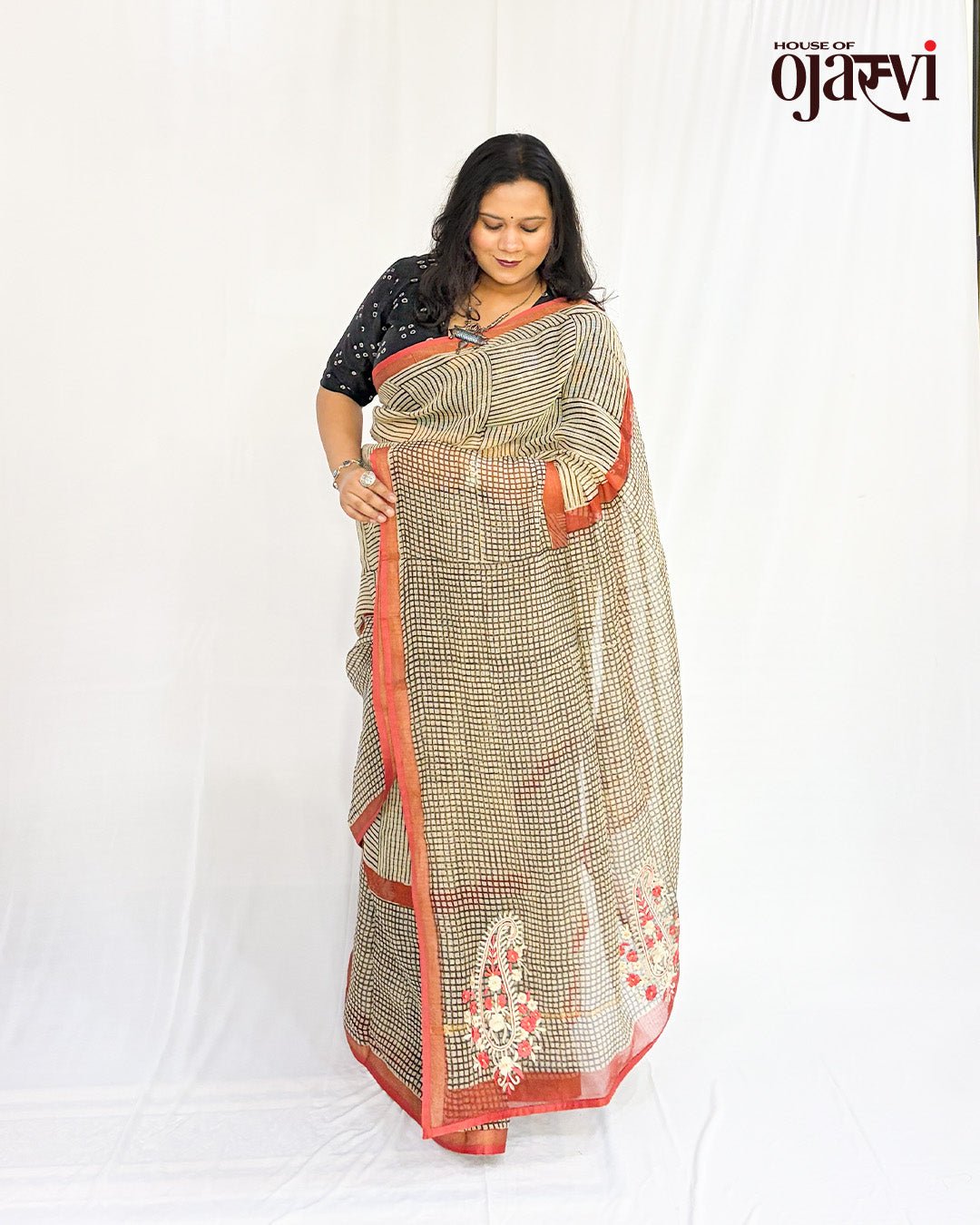 Woman wearing a beige and black check pattern Kota Doria handwoven saree with red border and embroidered paisley pallu by House of Ojasvi