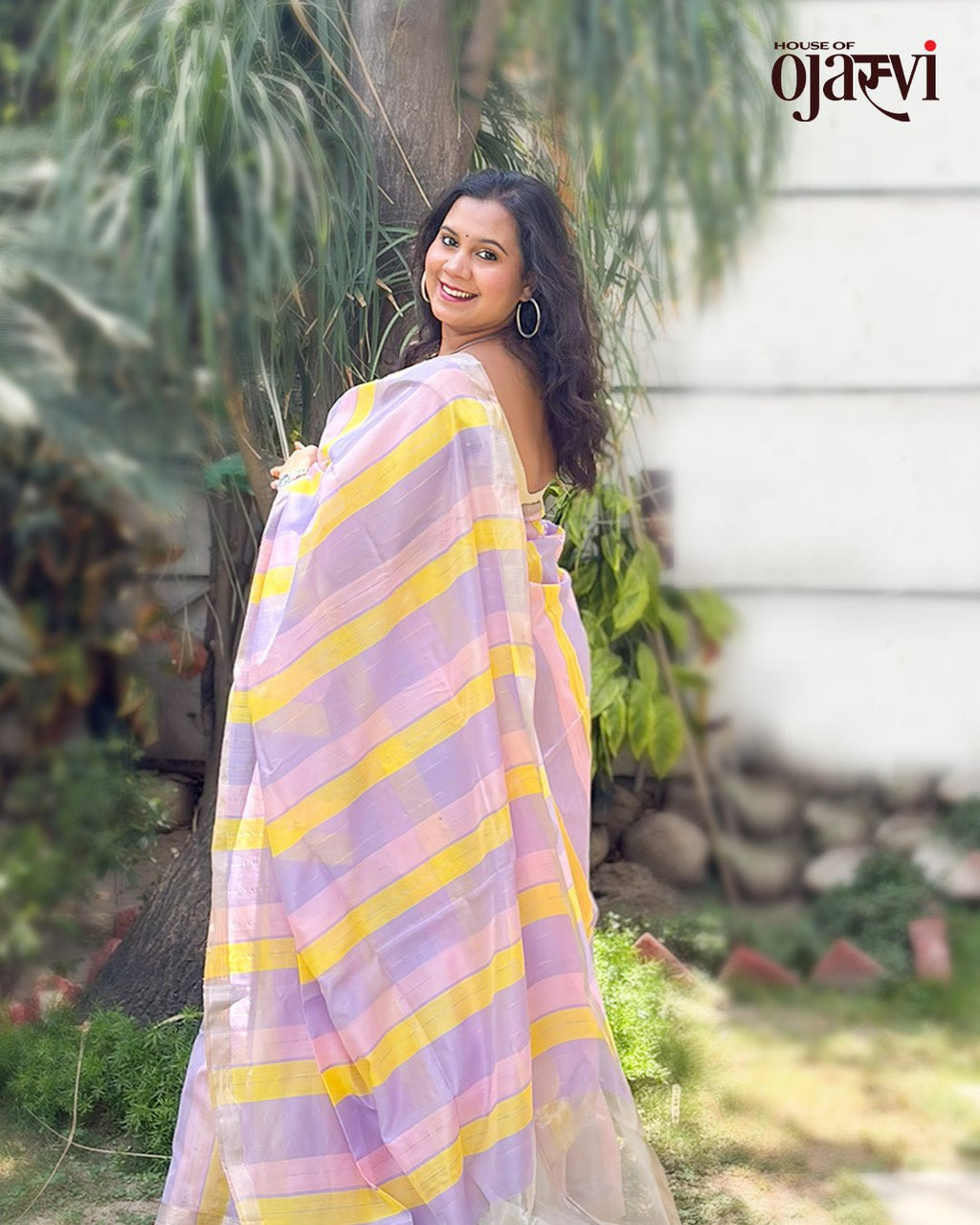 Model posing outdoors wearing the lavender and yellow striped handwoven Maheshwari saree by House of Ojasvi.