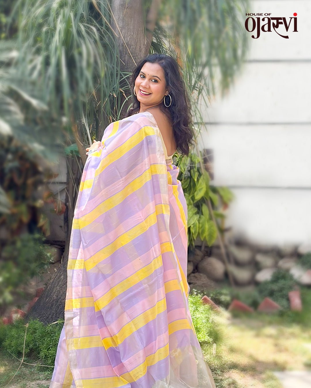 Model posing outdoors wearing the lavender and yellow striped handwoven Maheshwari saree by House of Ojasvi.