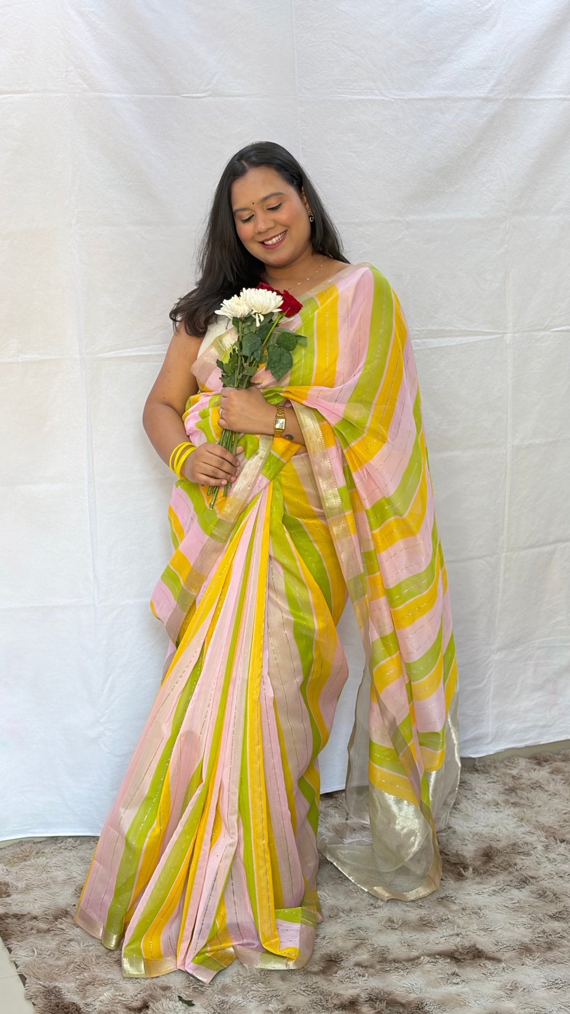 Model holding flowers while wearing the light pink, yellow, and green striped Maheshwari handwoven saree by House of Ojasvi.