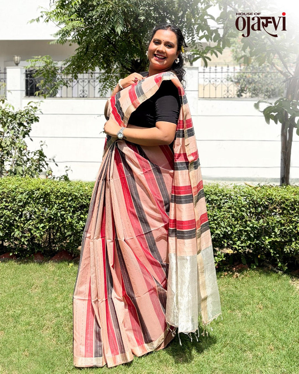 Garden view of a model styling the maroon and neutral striped Maheshwari handwoven saree with a zari pallu.