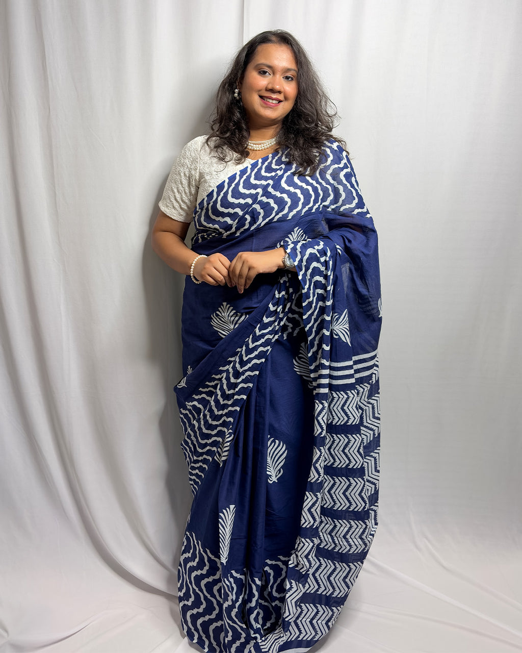 Full-length front view of the navy blue and white block-print cotton handwoven saree styled with a white blouse and pearl jewellery