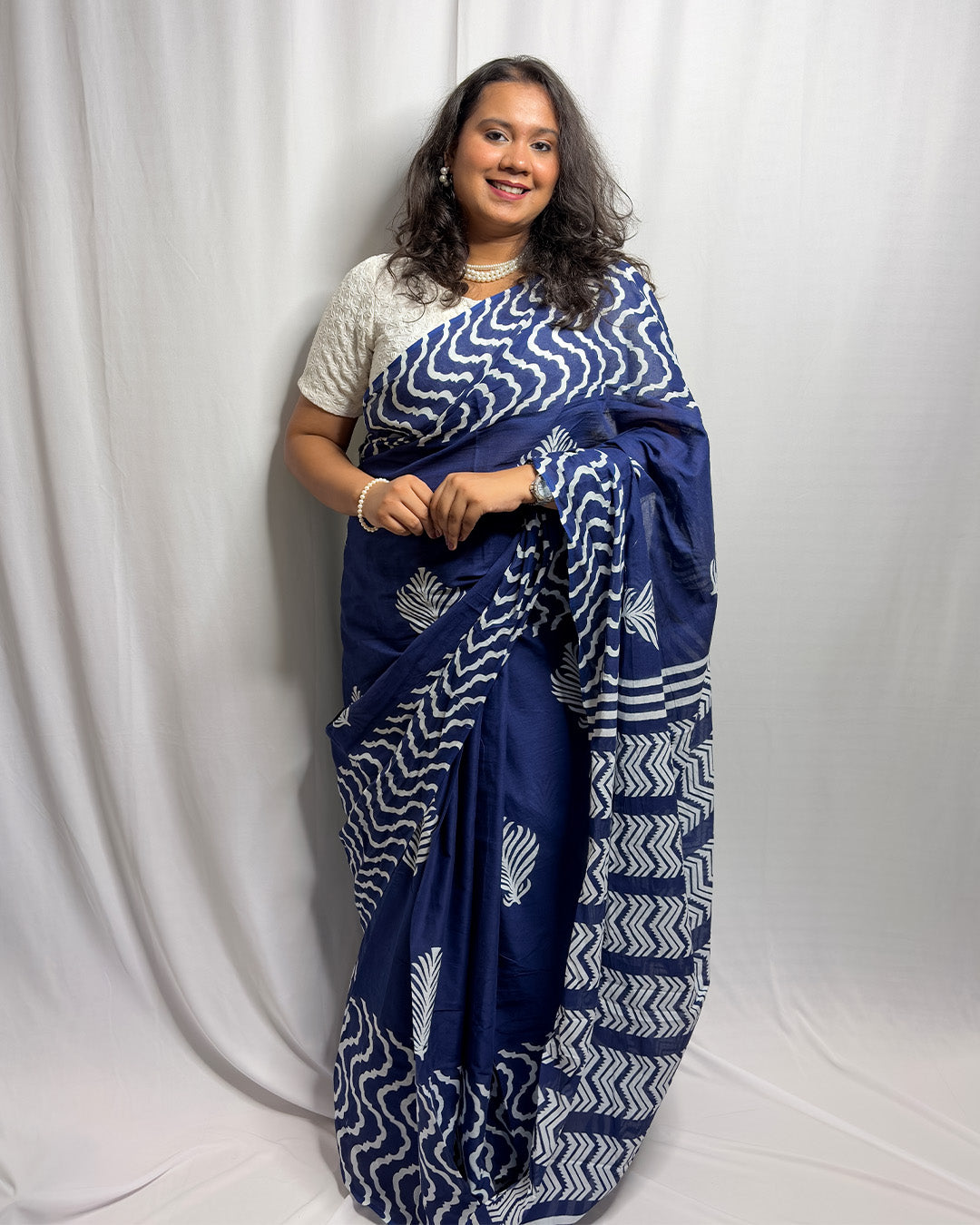 Full-length front view of the navy blue and white block-print cotton handwoven saree styled with a white blouse and pearl jewellery