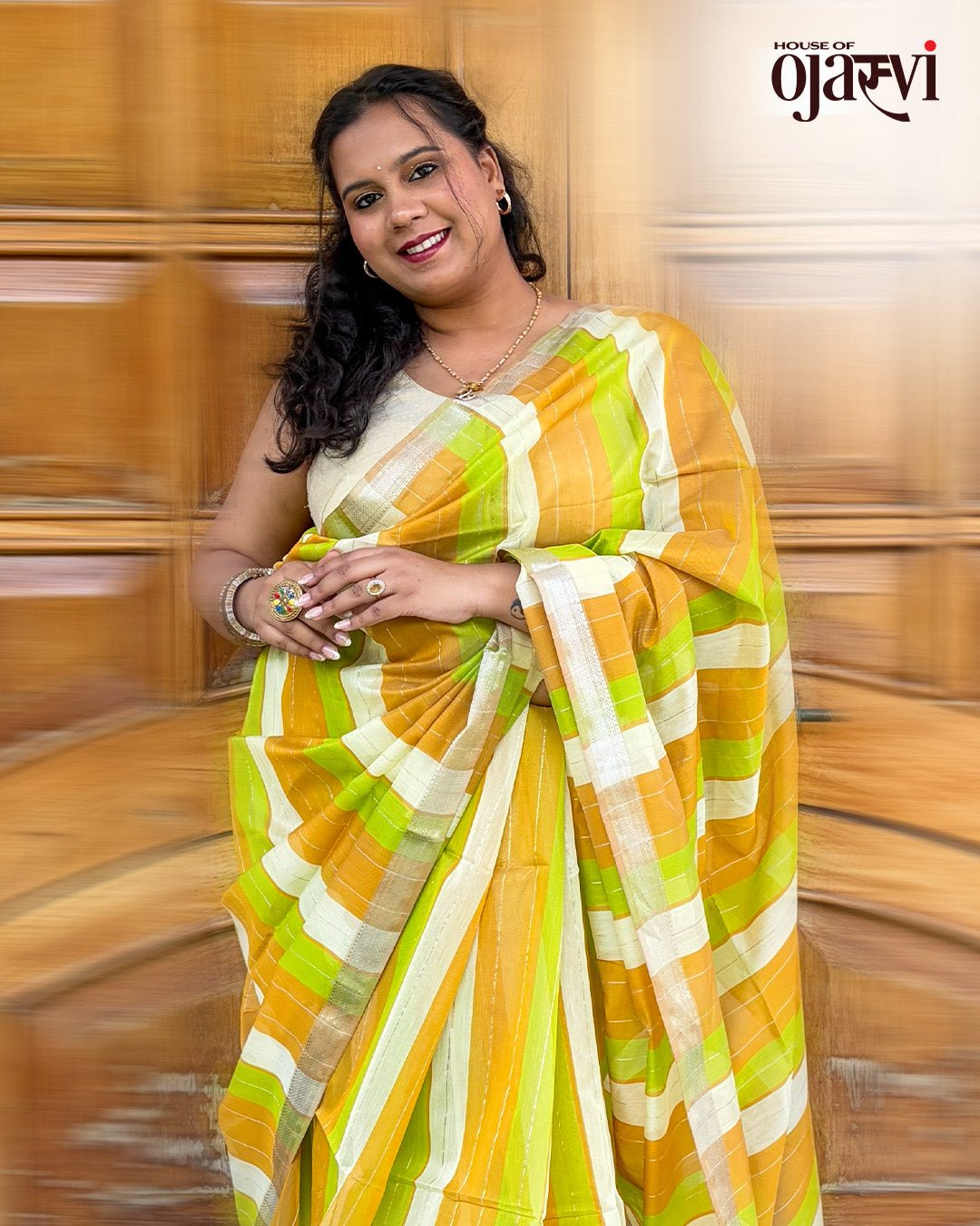 Full drape view of the orange, lime green, and cream striped Maheshwari handwoven saree against a wooden door background.