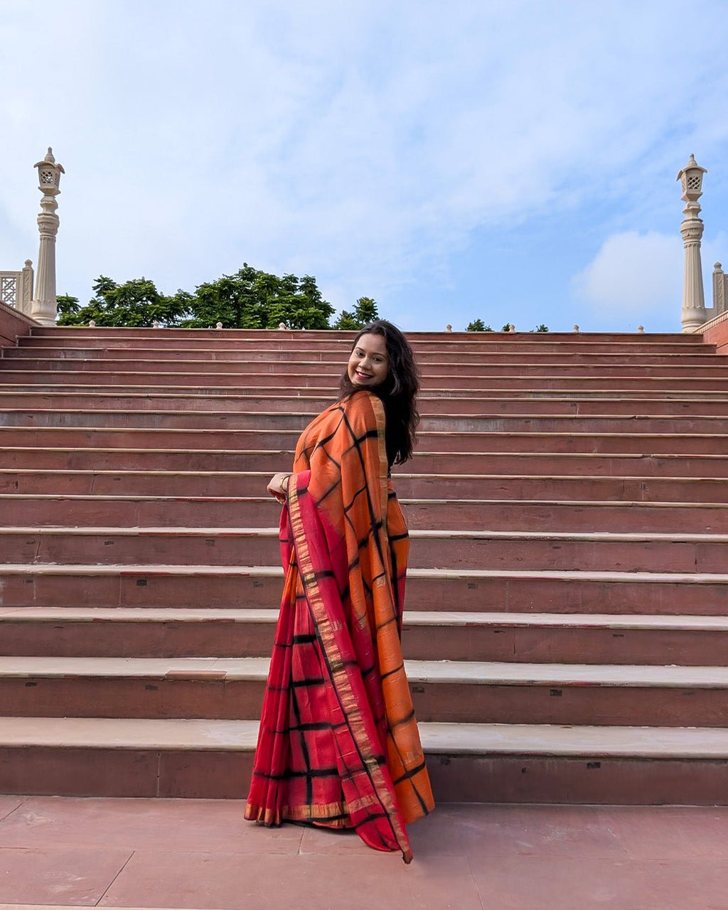 Full drape view of the orange and red checked Maheshwari handwoven saree with traditional gold zari borders.