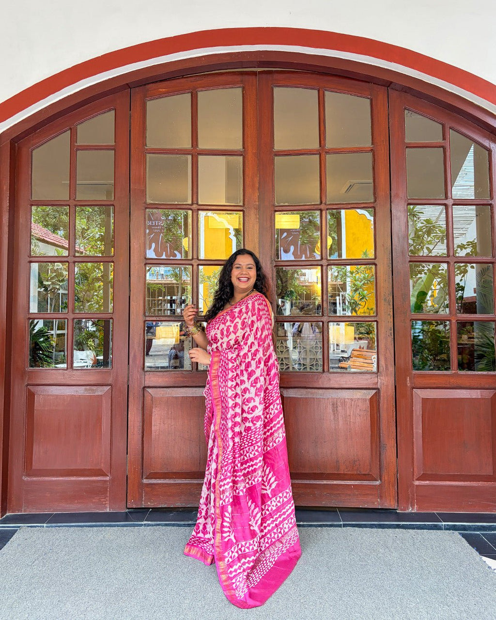Lifestyle view of a model sitting on a wooden bench wearing the pink and white block-print Maheshwari saree.