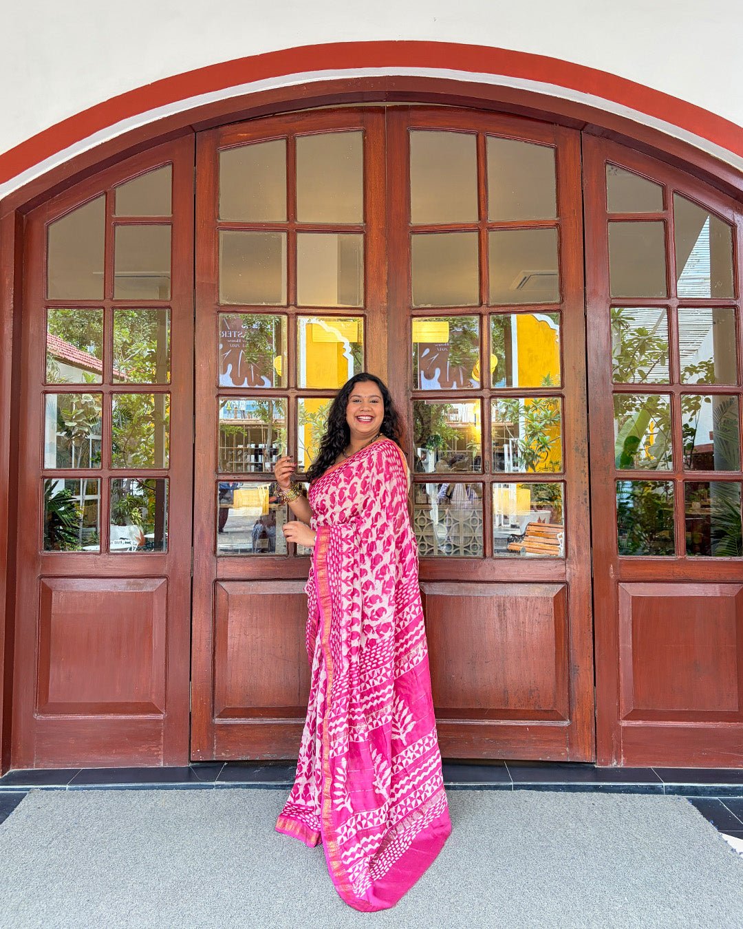 Lifestyle view of a model sitting on a wooden bench wearing the pink and white block-print Maheshwari saree.