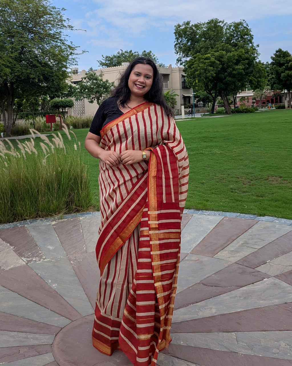 Full drape view of the red and cream striped Maheshwari handwoven saree in an outdoor garden setting.