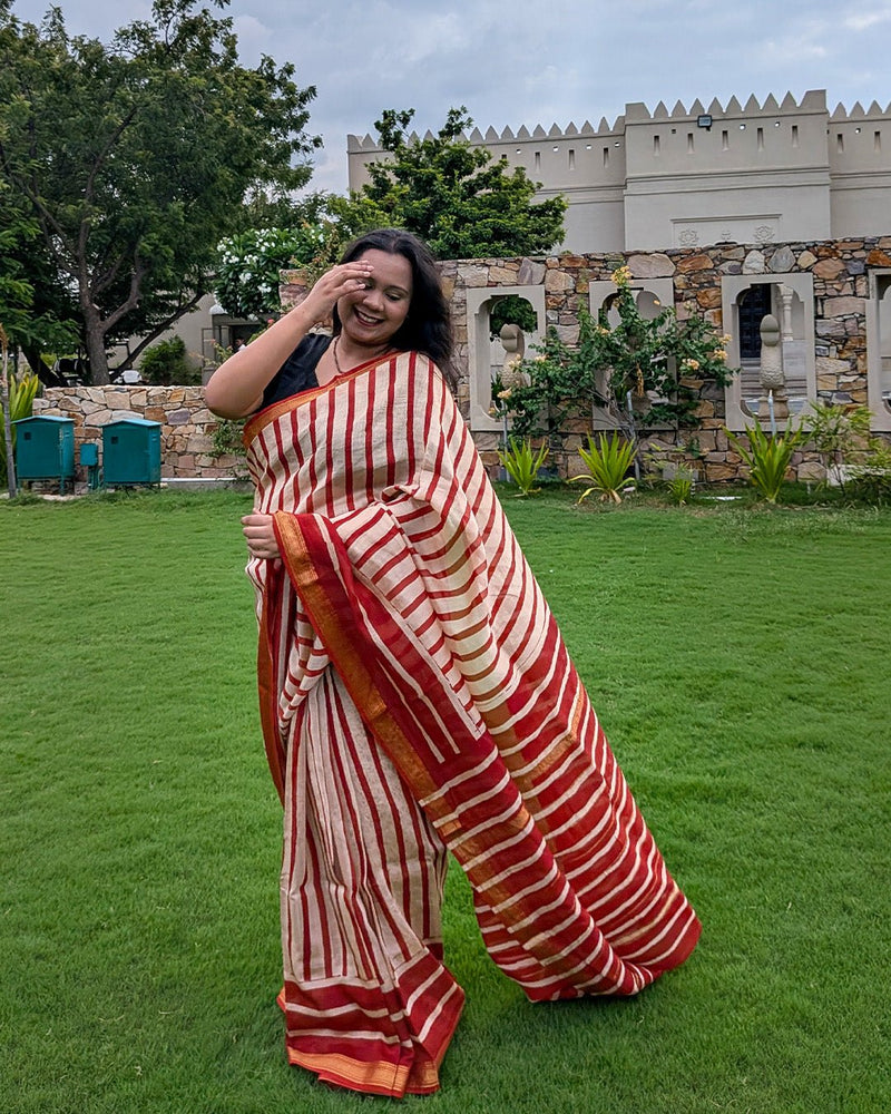 Model posing gracefully against a wooden doorway wearing the red and cream striped Maheshwari handwoven saree by House of Ojasvi.