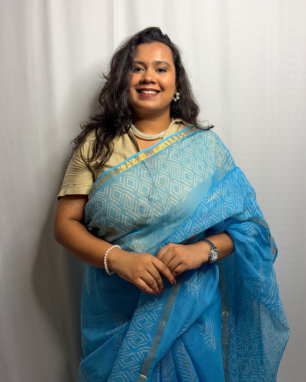 Model wearing the sky blue block-print handwoven Kota Doria saree with a beige collared blouse and pearl jewellery by House of Ojasvi