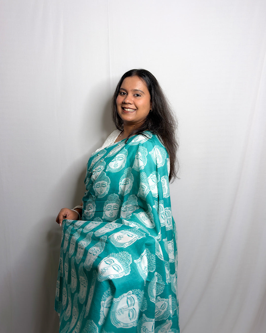 Side drape view of the teal green and white Buddha print cotton handwoven saree showing the solid teal pleats and printed pallu